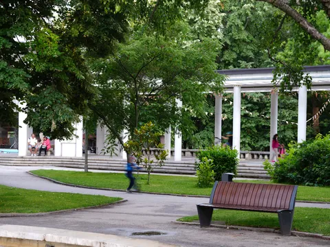 Бялата колонада в парка, пейка и зелени лехи пред нея