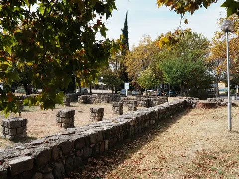 Дългият каменен зид и базите на колоните на базиликата, встрани алея с лампа