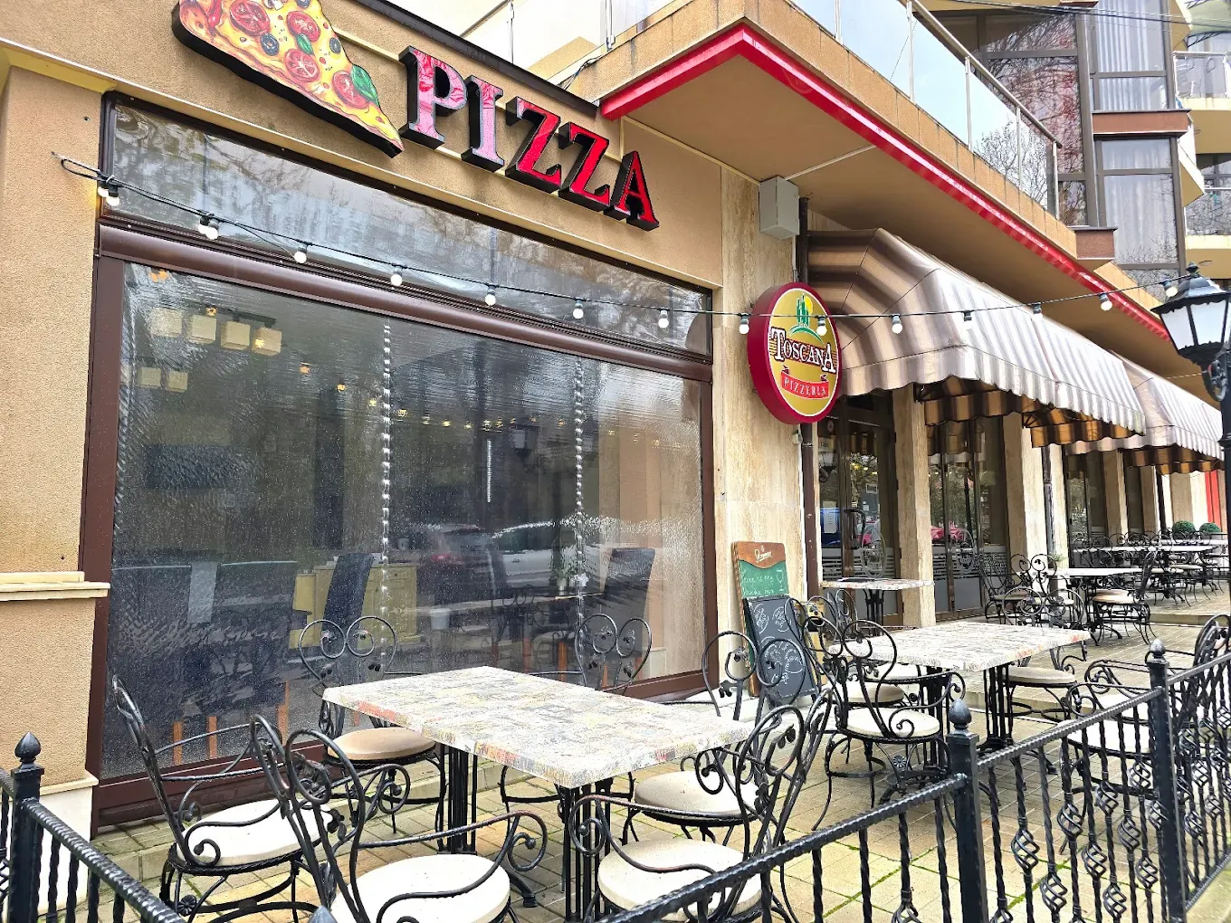 Фасадата на Пицария Тоскана с надпис „Pizza“ и маси на тротоара