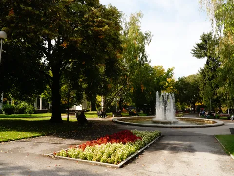Фонтанът в парка и цветна леха под високите дървета