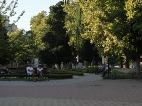 Хора на пейки в градския парк на Хисаря, цветни лехи и фонтан в дъното