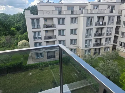 Изглед от остъклен балкон към жилищна сграда и зеленина в двора