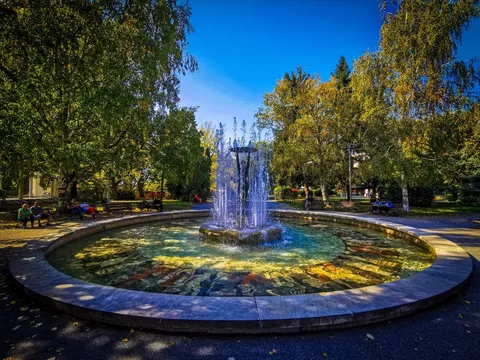Кръглият басейн на фонтана с мозаечно дъно и водни струи сред есенни дървета