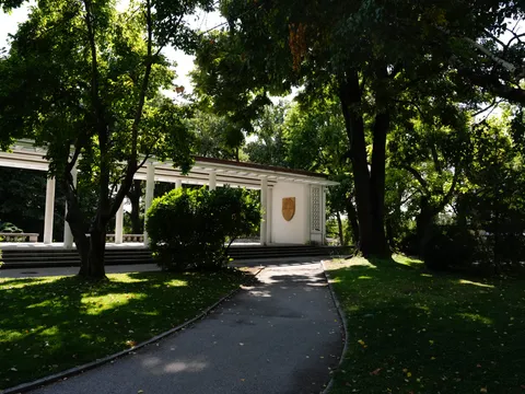 Алея към бялата колонада с герба на града, сред дърветата