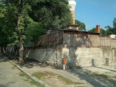 Минарето на джамията в Хисаря зад дървета и стара ограда край улицата