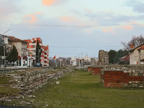 Ниски основи на крепостната стена в тревата покрай улица с къщи