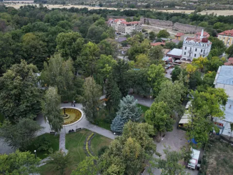Парк с кръгла цветна леха и бяла сграда с купол, гледка от въздуха