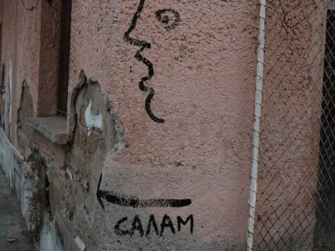 Профил на лице и надпис „Салам“ със стрелка, нарисувани на розова стена