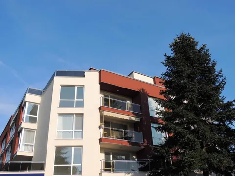 Сградата с апартаментите и висок бор до нея под синьо небе