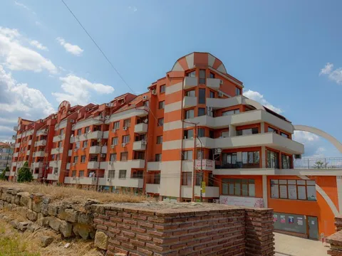 Жилищната сграда с оранжева фасада и полукръгъл покрив над древни каменни зидове
