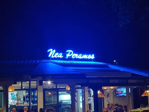 Светещият син надпис „Nea Peramos“ над терасата на ресторанта вечер