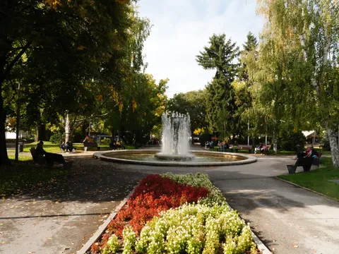 Цветна леха с червени и бели цветя пред фонтана в парка
