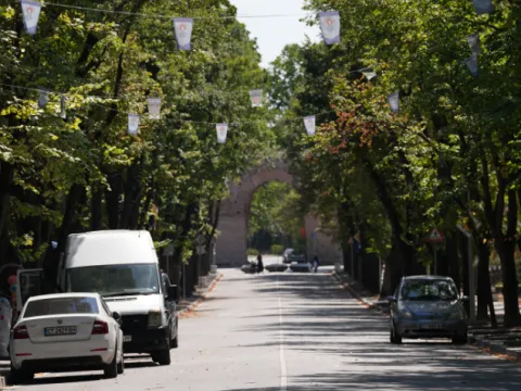 Улица под сенчести дървета с флагчета, в дъното тухлена арка
