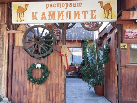 Входът на Ресторант Камилите с табела с камили и колело от каруца
