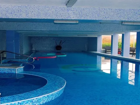 Закрит басейн с кръгло джакузи и големи прозорци към двора
